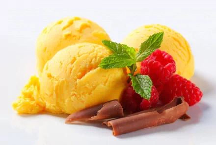 Three scoops of vibrant yellow ice cream are garnished with fresh raspberries and a sprig of mint, accompanied by rich chocolate curls, creating a delightful food-themed HD desktop wallpaper.