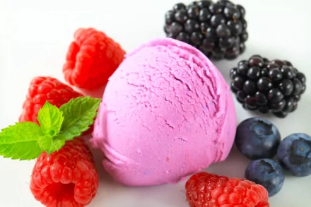 A vibrant scoop of pink ice cream surrounded by fresh raspberries, blackberries, and blueberries, set against a clean background, making for an enticing HD desktop wallpaper.