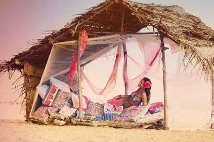 Ana Beatriz Barros lounges on colorful cushions inside a rustic, thatched beach hut with sheer white drapes in this 4K Ultra HD PC desktop wallpaper.