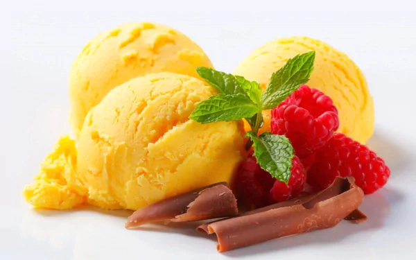 Three scoops of vibrant yellow ice cream are garnished with fresh raspberries and a sprig of mint, accompanied by rich chocolate curls, creating a delightful food-themed HD desktop wallpaper.