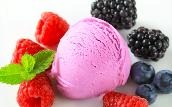 A vibrant scoop of pink ice cream surrounded by fresh raspberries, blackberries, and blueberries, set against a clean background, making for an enticing HD desktop wallpaper.