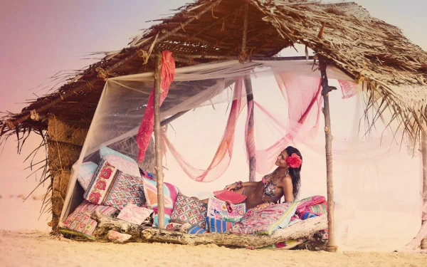 Ana Beatriz Barros lounges on colorful cushions inside a rustic, thatched beach hut with sheer white drapes in this 4K Ultra HD PC desktop wallpaper.