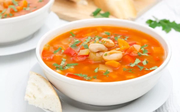 A vibrant bowl of soup with colorful vegetables and herbs, accompanied by a slice of bread. This HD image serves as a warm and inviting desktop wallpaper background.