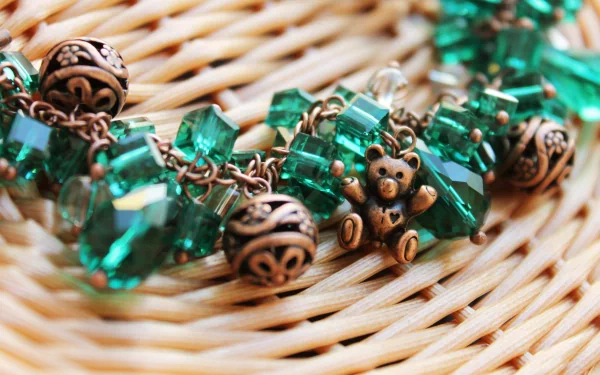 Close-up of intricate jewelry featuring green crystals and a charming teddy bear charm, set against a woven background, creating a vibrant and artistic 4K Ultra HD wallpaper.