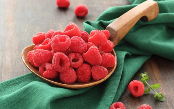 HD desktop wallpaper featuring fresh raspberries overflowing from a wooden spoon on a green cloth, highlighting vibrant red fruit in a rustic setting.
