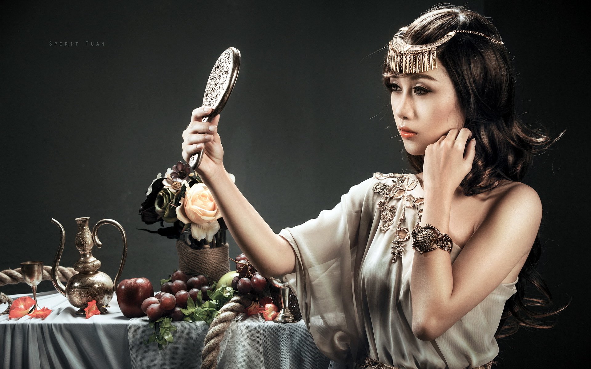 HD PC desktop wallpaper featuring woman Quỳnh Nhi dressed in elegant, vintage-inspired attire, holding a hand mirror beside a table with fruits and antique items.