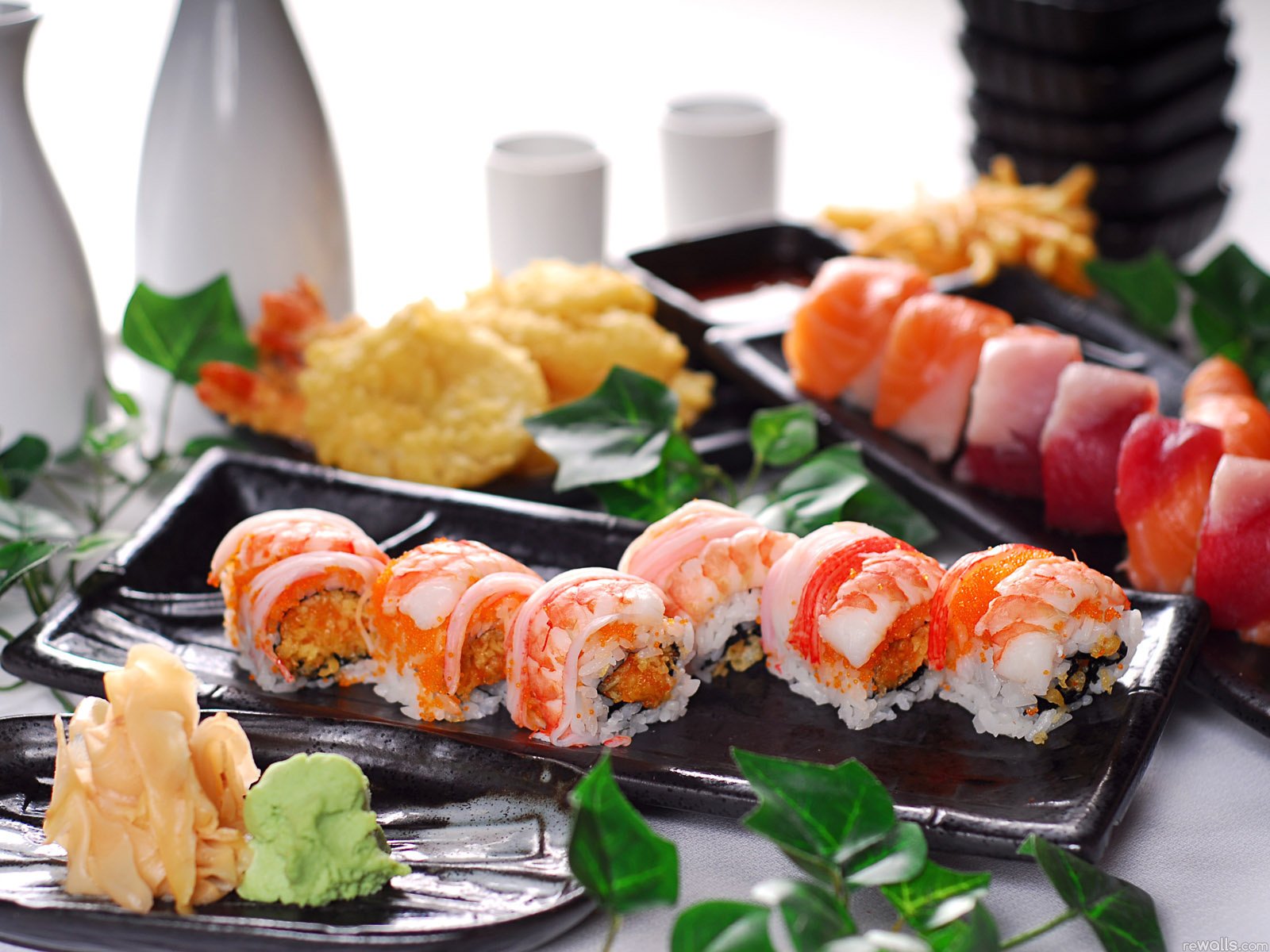 A vibrant display of assorted sushi rolls on sleek black plates, accompanied by tempura and garnished with green leaves, creating an appetizing HD desktop wallpaper for food enthusiasts.