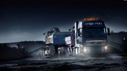 HD desktop wallpaper featuring a Volvo 700 truck hauling heavy machinery through a rugged, dark landscape at night.