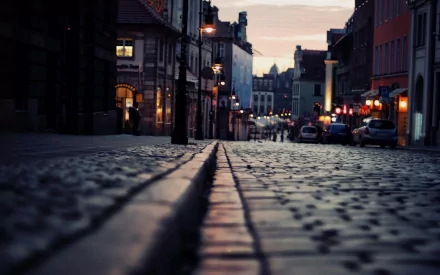 HD desktop wallpaper of a cobblestone road illuminated by streetlights in the night, lined with buildings, creating an atmospheric cityscape.
