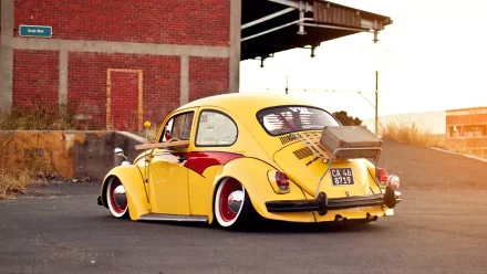 A vibrant yellow Volkswagen Beetle with artistic detailing is parked against a rustic brick background, making it a striking HD desktop wallpaper and background option.