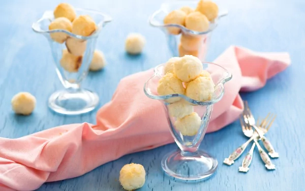 A vibrant HD desktop wallpaper featuring elegant glass dessert cups filled with round, creamy treats, set on a soft pink cloth against a light blue background.