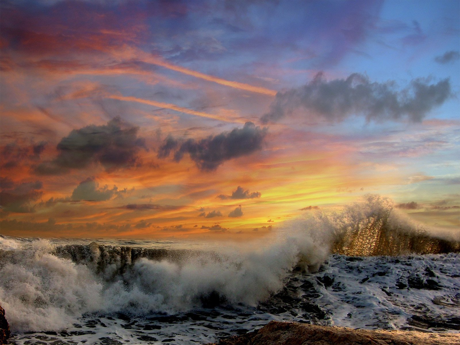 HD PC desktop wallpaper: dramatic ocean wave crashing under a fiery sunset sky, vivid clouds and spray in a nature scene background.
