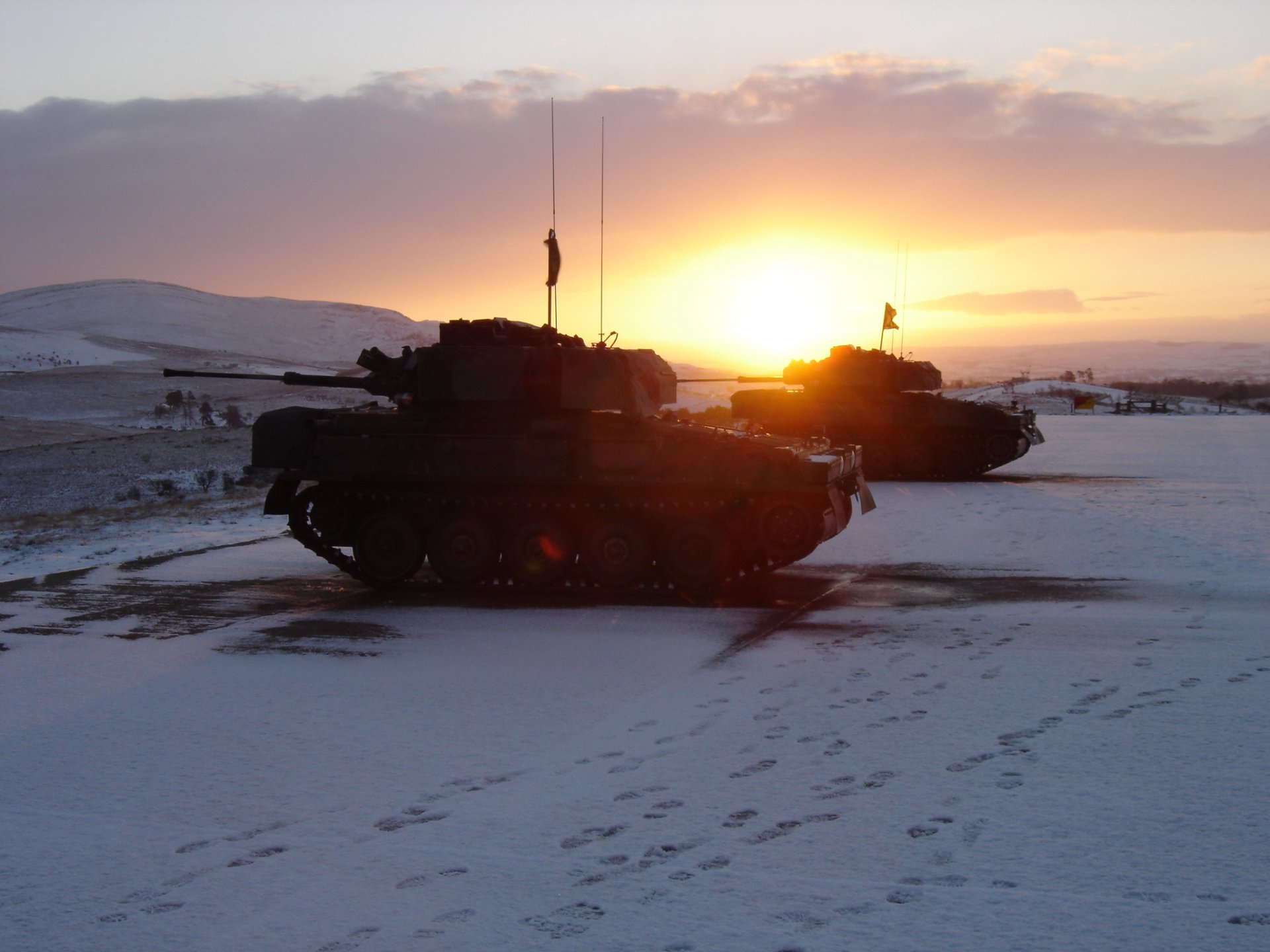 HD military desktop wallpaper featuring tanks silhouetted against a vibrant sunset on a snowy terrain.
