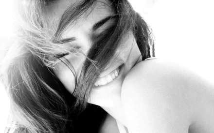 Black-and-white HD desktop wallpaper featuring a smiling Adriana Lima with hair partially covering her face, exuding natural beauty and warmth.