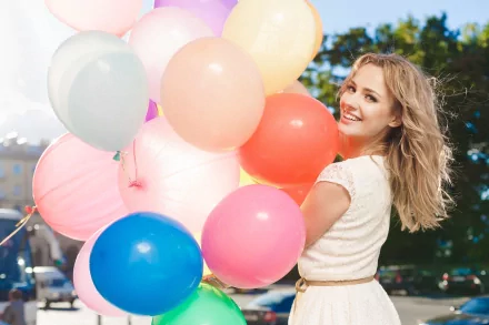 A woman joyfully holds a bunch of colorful balloons on a sunny day. This high-definition image makes for a vibrant and uplifting desktop wallpaper and background.