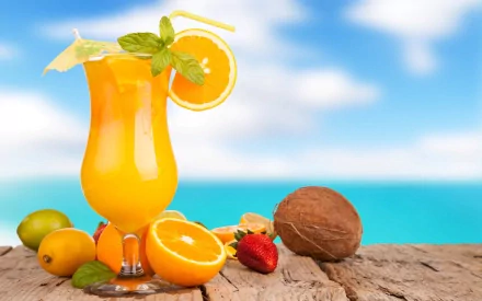HD PC desktop wallpaper featuring a vibrant orange cocktail garnished with mint and citrus, set on a wooden surface with tropical fruits and a blurred ocean background.