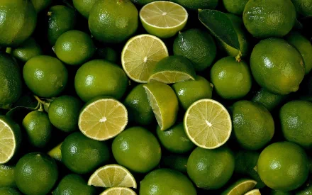 A vibrant HD wallpaper featuring a collection of fresh limes, whole and sliced, showcasing their bright green color and texture against a dark background.