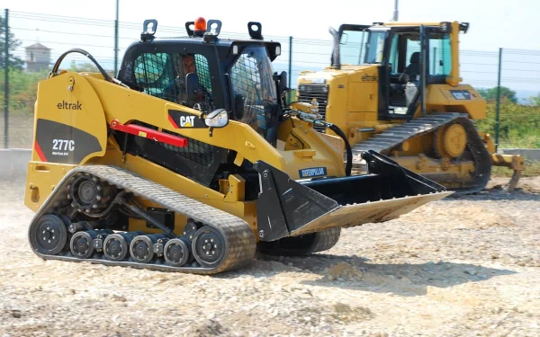 HD PC desktop wallpaper: Caterpillar Inc. construction vehicles — yellow Caterpillar 277C compact track loader in foreground with a larger tracked excavator/bulldozer behind on gravel.
