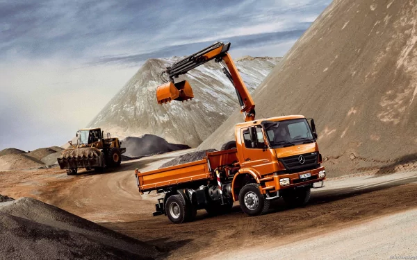 HD desktop wallpaper featuring an orange Mercedes-Benz excavator vehicle working on a construction site with large dirt mounds and a loader in the background.