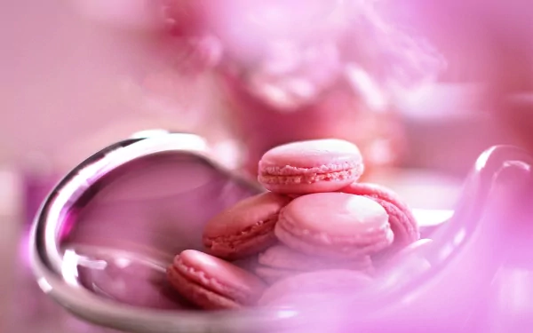A close-up of delicate pink macarons arranged in a shiny bowl, surrounded by soft pink hues, creating an elegant food-themed 4K Ultra HD desktop wallpaper.