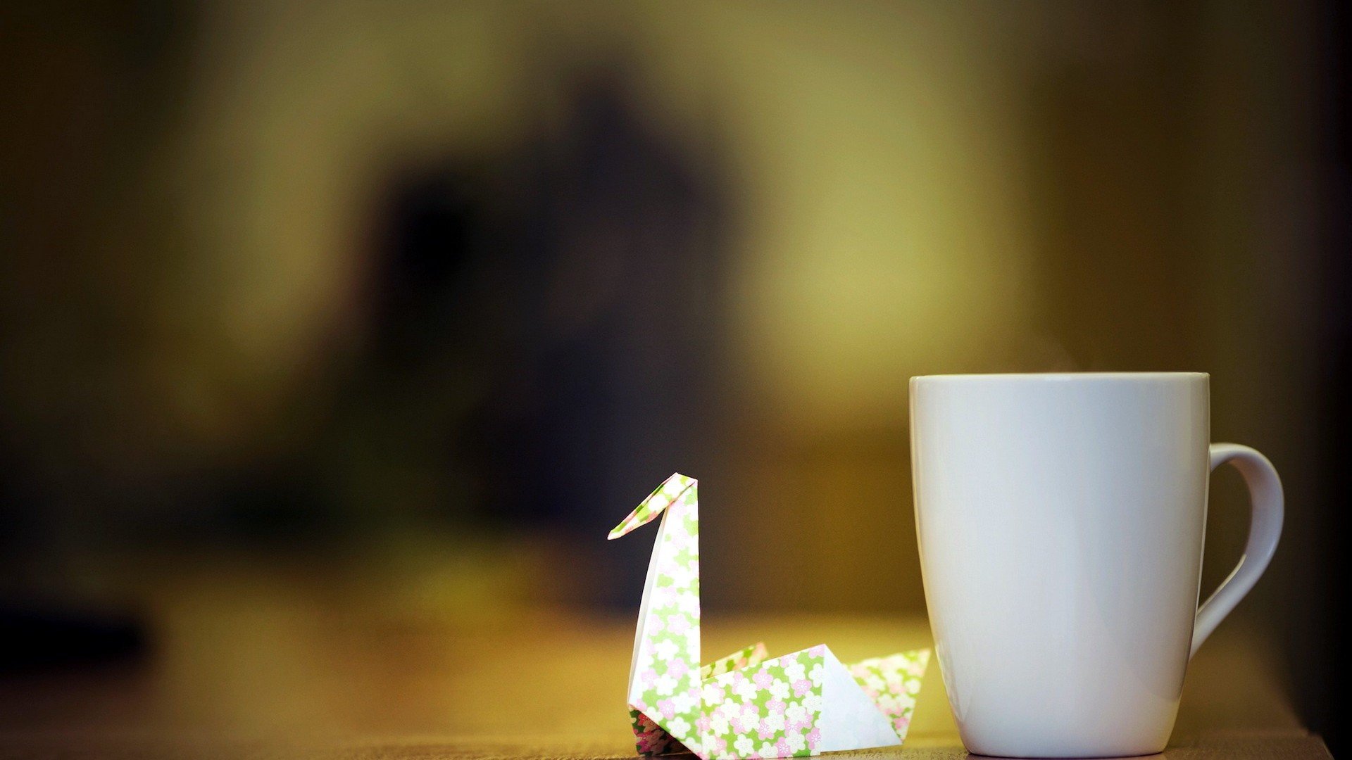 HD PC desktop wallpaper featuring a man-made origami swan beside a white coffee mug, set against a softly blurred background with warm lighting.
