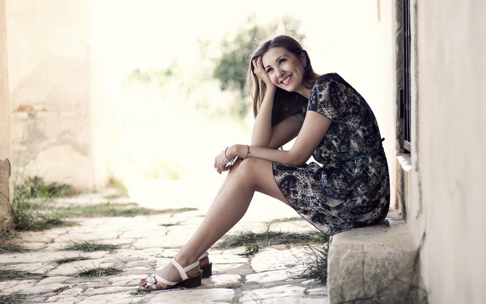 A woman sitting thoughtfully in a sunlit alley, exuding a relaxed mood, captured as a high-definition desktop wallpaper and background.