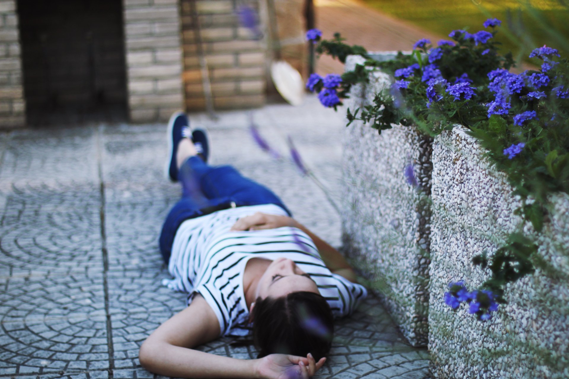 A woman lies peacefully on a textured surface surrounded by purple flowers, capturing a serene mood. This HD wallpaper enriches any desktop background with its calming ambiance.