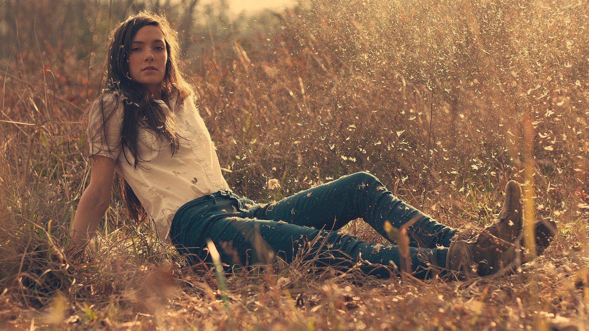 A woman with long hair lounges in a sunlit field, surrounded by tall grasses. The image exudes a serene mood and serves as an HD desktop wallpaper and background.