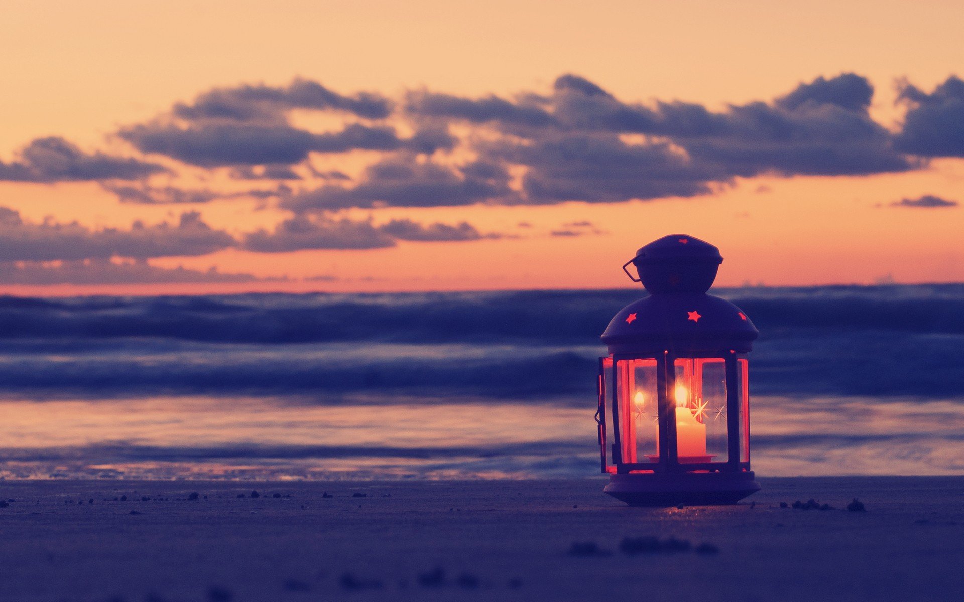 A serene beach scene at sunset featuring a glowing lantern, with gentle waves and soft clouds in the background—an evocative HD desktop wallpaper capturing tranquility.