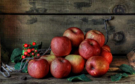 A vibrant collection of red apples rests against a rustic wooden background, complemented by green leaves and small berries, creating an appealing HD desktop wallpaper.