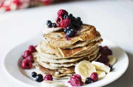 A stack of fluffy pancakes topped with raspberries, blueberries, and banana slices on a white plate, captured in HD for a vibrant desktop wallpaper.
