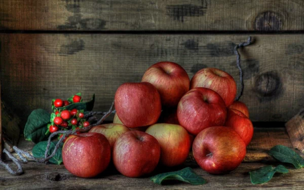 A vibrant collection of red apples rests against a rustic wooden background, complemented by green leaves and small berries, creating an appealing HD desktop wallpaper.