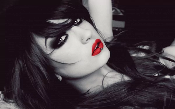 HD desktop wallpaper featuring a woman with black hair, piercing, and bold red lipstick, exuding a striking mood. The close-up showcases her face in detail, creating a captivating and dramatic background.