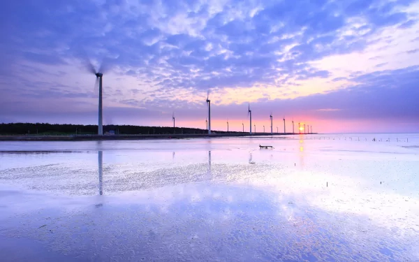 HD desktop wallpaper featuring a serene coastal scene with man-made wind turbines silhouetted against a colorful sunset sky and reflected in calm water.