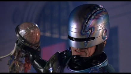 HD PC desktop wallpaper featuring RoboCop from the movie RoboCop 2, showcasing the iconic armored cyborg in a dimly lit setting holding a damaged robotic head.