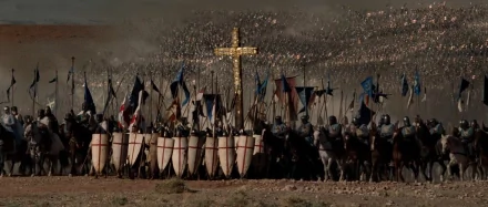 HD PC desktop wallpaper: battle scene from the movie Kingdom of Heaven — crusader shield wall with banners and a large golden cross rising above a dusty battlefield.