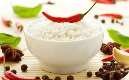 A white bowl of rice topped with a red chili pepper, surrounded by various herbs and spices, creates an inviting food-themed HD wallpaper for PC desktops.