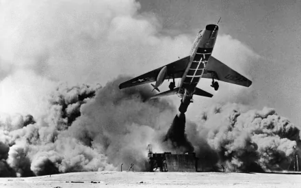 HD PC desktop wallpaper: black-and-white image of a North American F-100 Super Sabre military jet climbing through a billowing cloud of smoke and dust.