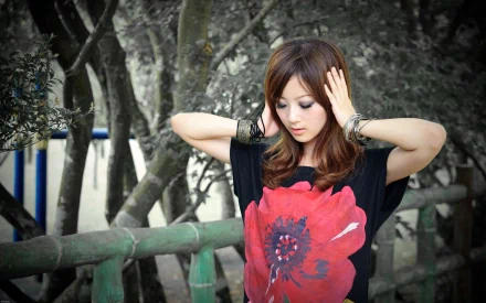 HD desktop wallpaper of a woman with brown hair wearing a black top featuring a large red flower, set against a grayscale background of trees and wooden railings.