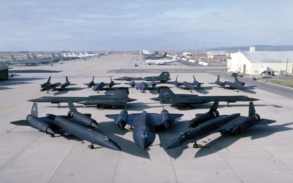 An aerial view of multiple Lockheed SR-71 Blackbird aircraft arranged on a tarmac, showcasing their sleek design and dark coloration against a backdrop of military hangars.