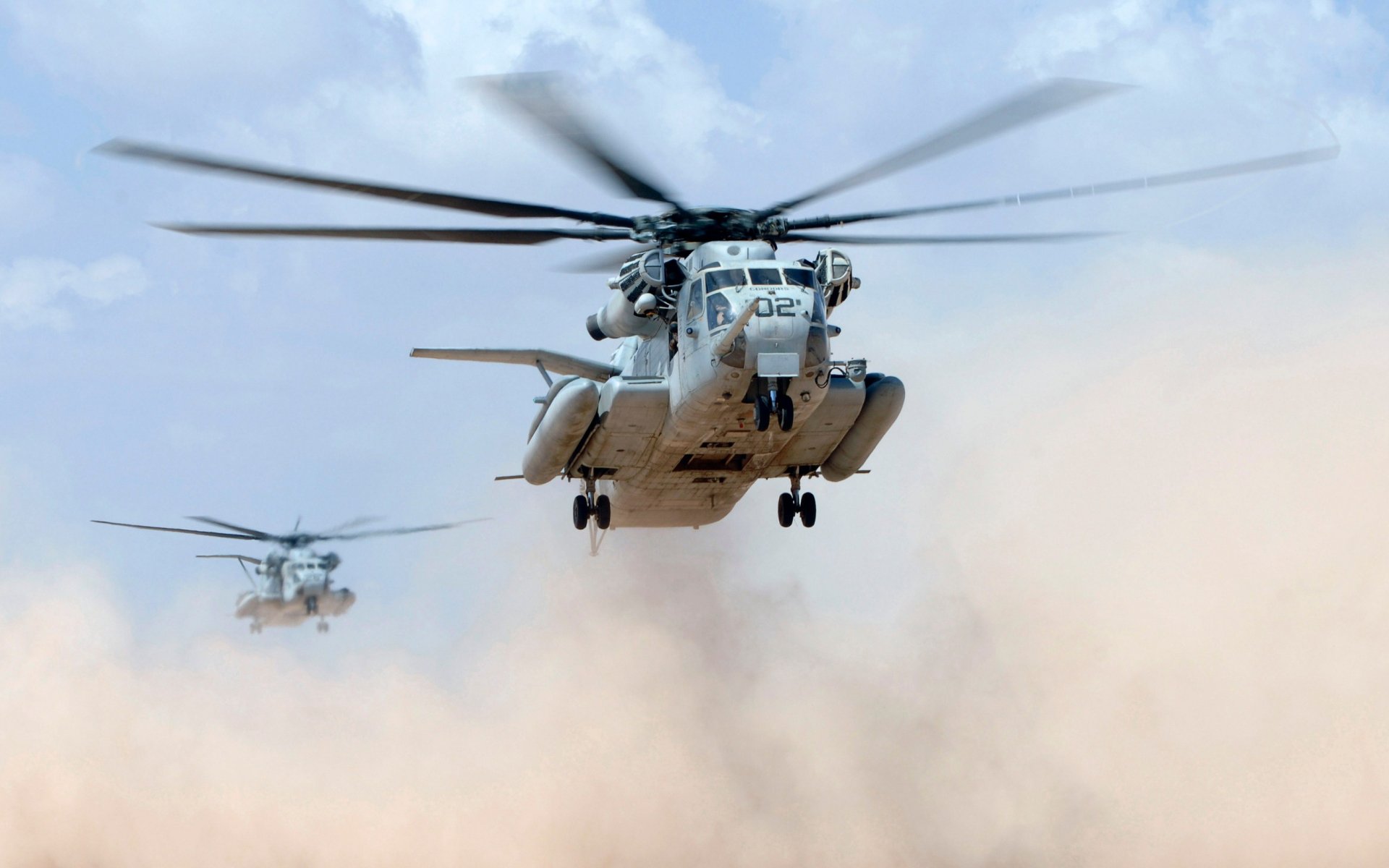 HD desktop wallpaper featuring two military Sikorsky MH-53 helicopters flying low over a dusty terrain with rotors in motion.