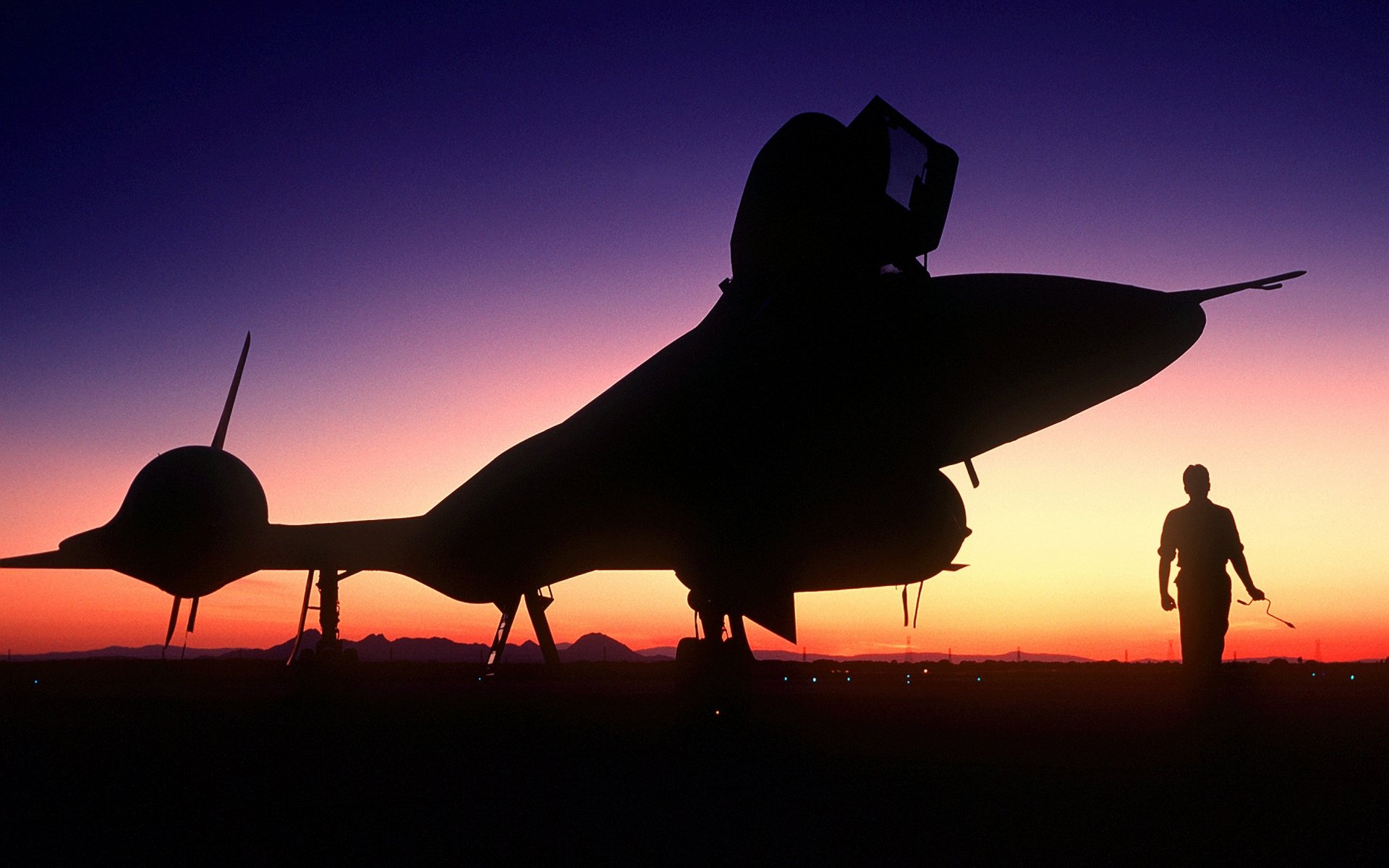 Silhouetted Lockheed SR-71 Blackbird military aircraft and a person at sunset, captured in an HD PC desktop wallpaper and background.