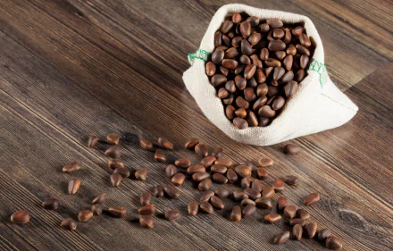 A burlap sack spilling roasted nuts onto a wooden surface, showcasing their rich brown color and texture, creating an appealing food-themed desktop wallpaper.