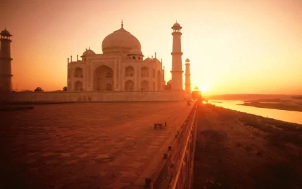 A stunning HD wallpaper of the Taj Mahal at sunset, showcasing its magnificent architecture against a warm, glowing sky and reflecting waters.