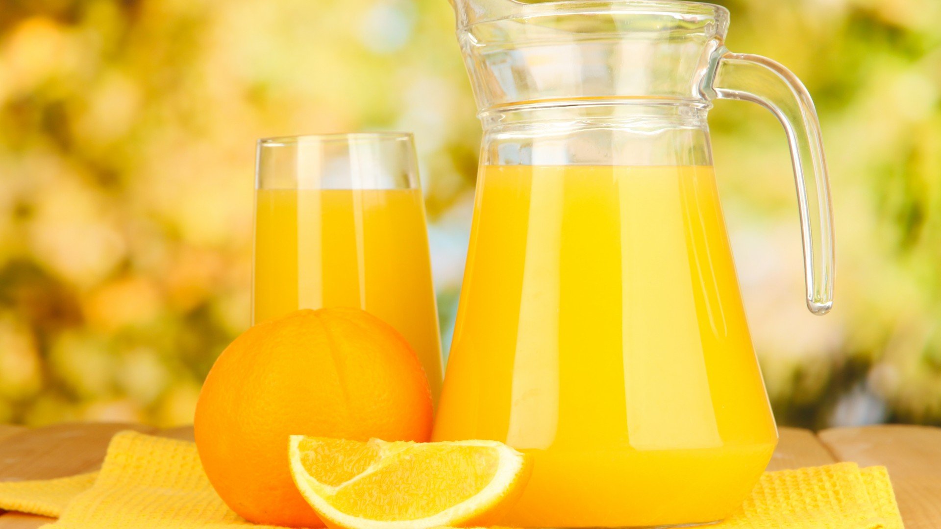 A refreshing display of orange juice in a pitcher and glass, accompanied by an orange and a slice, set against a warm, colorful background. HD PC desktop wallpaper.