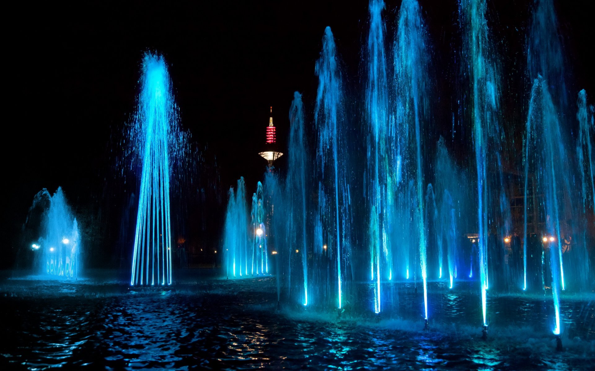A stunning HD desktop wallpaper featuring a vibrant man-made fountain illuminated by blue lights at night, creating a captivating water display against a dark backdrop.