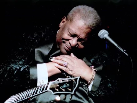 Music-themed HD PC desktop wallpaper of an older blues guitarist cradling his guitar by a microphone, eyes closed in a soulful performance.