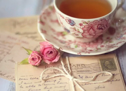 A delicate porcelain teacup filled with tea sits next to vintage postcards and pink roses, creating a serene food and tea-themed HD desktop wallpaper.