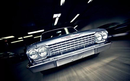HD PC desktop wallpaper featuring a close-up, dynamic shot of a classic Chevrolet vehicle with bright headlights in a motion-blurred garage setting.