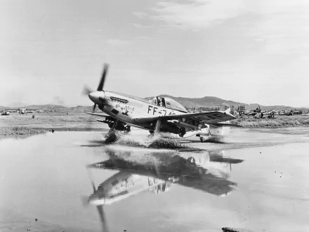Black and white HD desktop wallpaper showing a North American P-51 Mustang military aircraft taxiing on a wet runway with its reflection visible.